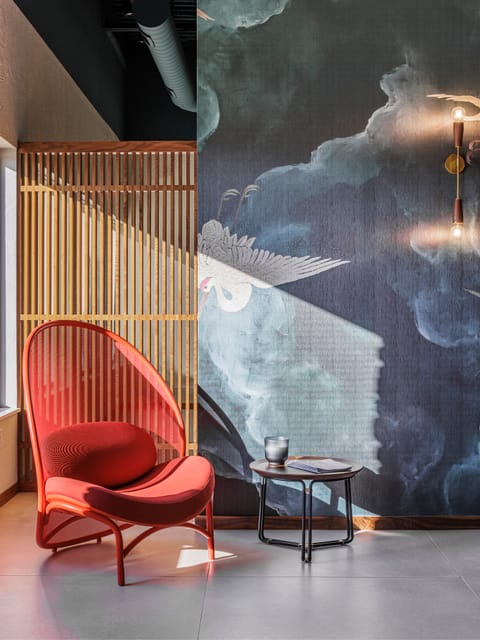 Red lounge chair beside a wood slat screen and crane mural wall